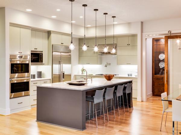 Row of glass pendant lights over a long marble kitchen island with bar stools