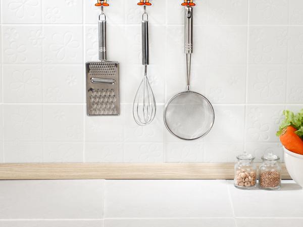 White kitchen wall tile with white grout behind a grater, whisk and strainer